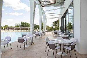 圣乔瓦尼-因马里尼亚诺海滨高尔夫度假酒店的一间设有白色桌椅的餐厅,位于游泳池旁