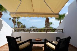 卡门港Playa Grande Puerto del Carmen Share Pool By PVL的阳台配有两把椅子和一张桌子,并种植了棕榈树