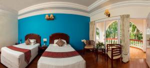 坦贾武尔GReaT Trails Riverview Thanjavur By GRT Hotels的一间卧室设有两张床、一张桌子和蓝色的墙壁