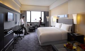 胡志明市西贡宾乐雅酒店的一间酒店客房,配有一张床,一个男人站在桌子旁