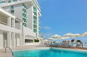 坎昆Oleo Cancun Playa All Inclusive Resort的游泳池位于带桌子和遮阳伞的大楼旁