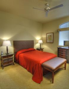 土桑Casitas at Sabino Springs的一间卧室配有红色的床、两张桌子和风扇