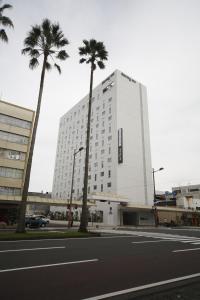 宫崎特嫩温泉云加诺玉宫崎多米经济型酒店的一座高大的白色建筑,前面有棕榈树