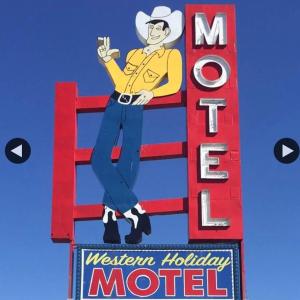 威奇托Western Holiday Motel的坐在长凳上的男人为汽车旅馆作标记