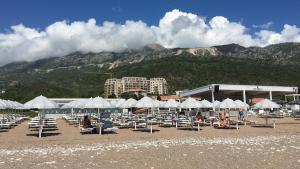 布德瓦ApartHotel Belvedere Residence Becici Budva的一个带椅子和白色遮阳伞的海滩和山