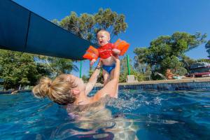 谢珀顿Shepparton Holiday Park and Village的把婴儿放在游泳池里的女人