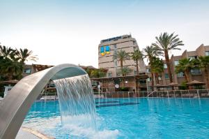 埃拉特埃拉特U珊瑚海滩俱乐部全包酒店的一座大楼前的游泳池,设有喷泉