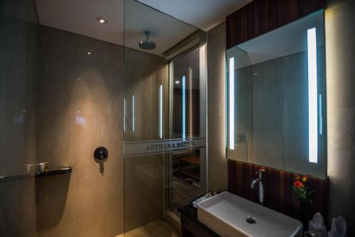 马卡萨Arthama Hotels Makassar的带淋浴、盥洗盆和镜子的浴室