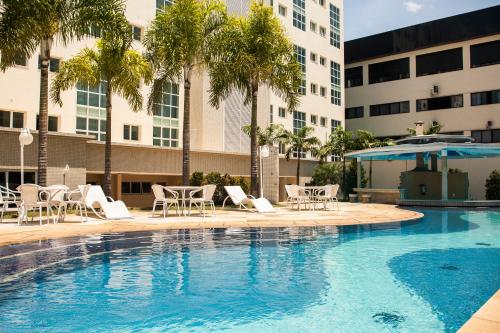 圣若泽杜斯坎普斯Hotel City Hall的一个带椅子和遮阳伞的游泳池,并种植了棕榈树