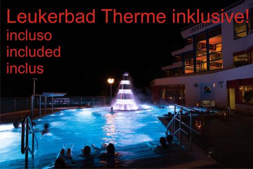 洛伊克巴德Hotel Paradis-Leukerbad-Therme的和水中的人一起在晚上使用游泳池