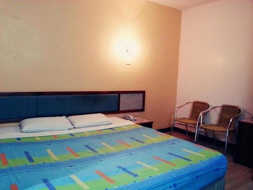 斗湖Monaco Dynasty Hotel的一间卧室配有一张带彩色床罩和两把椅子的床