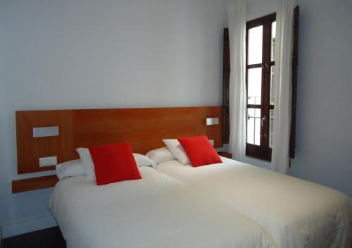 格拉纳达茂日旅行者公寓的卧室内配有两张带红色枕头的白色床。