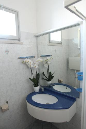 里米尼Hotel Giorg的浴室设有蓝色的柜台,配有两个水槽和鲜花