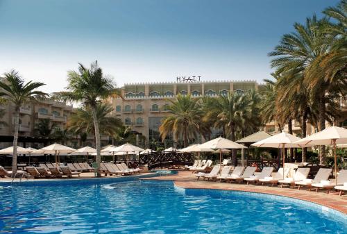 马斯喀特凯悦大酒店马斯喀特的一个带椅子和遮阳伞的游泳池以及酒店