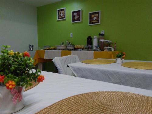 MaracanaúPousada das Maracanãs的绿色的客房配有带白色床单的桌子和鲜花