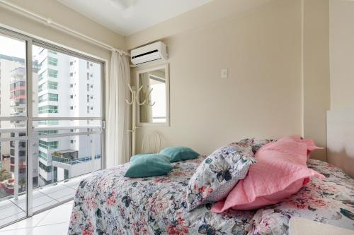 巴拉奈里奥-坎布里乌Apartamento Coral - 1 quadra do Mar的卧室配有带枕头的床铺和窗户。