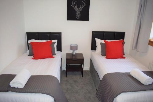 福尔柯克Kelpies Serviced Apartments- Russell的配有红色和白色枕头的客房内的两张床
