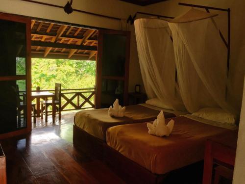 琅勃拉邦班微凡木屋旅馆的配有桌子和窗户的客房内的两张床