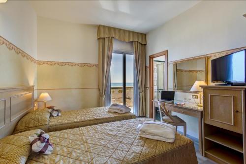 里米尼拜伦酒店的酒店客房设有两张床、一张桌子和一台电视。