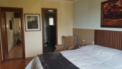 格拉玛多Apartamento Gramado的卧室配有一张白色大床和一把椅子