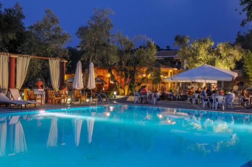 罗迪-加尔加尼科波吉欧德格里乌里维度假酒店的夜间游泳池,配有桌子和遮阳伞