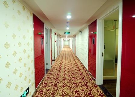 梅州尚客优连锁广东梅州梅县丽江湾店的一条带红色墙壁的走廊和一条铺有红色和金色地毯的长走廊