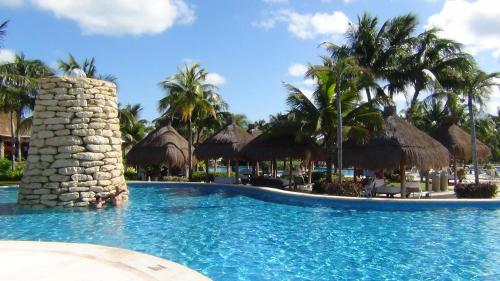 普拉亚卡门Suites at Mayan Palace Vidanta Resort Riviera Maya的棕榈树和草伞度假村的游泳池