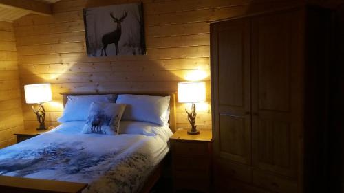 艾尔德里Lochinvar - Highland Log Cabin with Private Hot Tub的一间卧室配有一张带两盏灯的床,墙上挂着一张鹿的照片