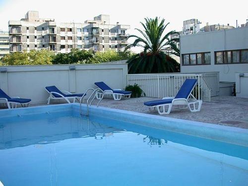门多萨Millenium Mendoza Apartments的一座带蓝色椅子的游泳池,位于大楼旁