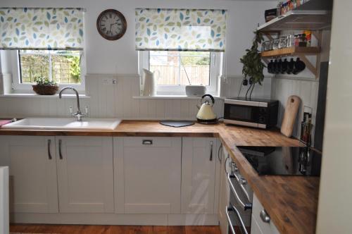 克利尔威尔Foxglove Cottage的厨房配有白色橱柜和木制台面
