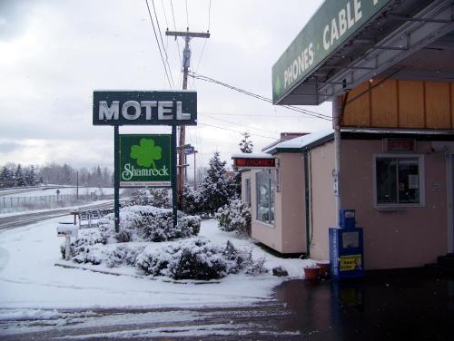 贝灵厄姆Shamrock Motel的商店旁边的雪地里的一个汽车旅馆标志