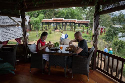 琅勃拉邦Shangri-Lao Resort的坐在门廊桌子上的男人和女人