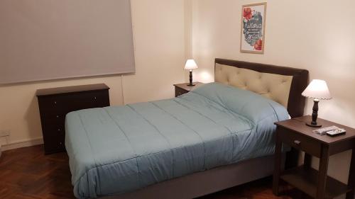 布宜诺斯艾利斯Departamento Obelisco的一间卧室配有一张带蓝色毯子的床和两张桌子