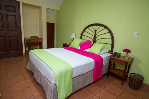 马那瓜Hotel Colibri的一间卧室配有一张大床,铺有粉色和绿色的床单。