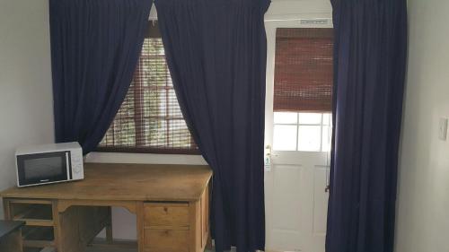 德班Pastel cottages的配有蓝色窗帘的窗户和带微波炉的书桌
