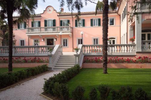 蒙特法尔科Villa Santa Barbara的一座大型粉红色的别墅,拥有棕榈树和草坪