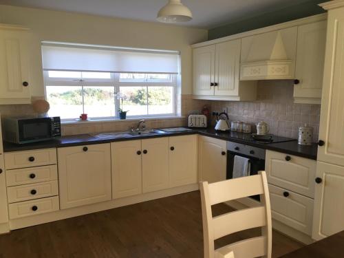 波特萨伦No 4 Ballymastoker Cottage的厨房配有白色橱柜、水槽和窗户。