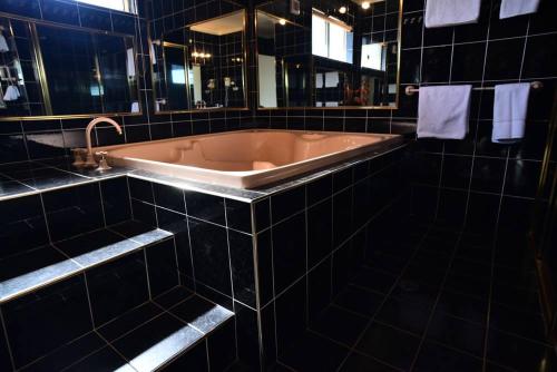 JuneeThe Crossing Motel的带浴缸的黑色瓷砖浴室设有水槽