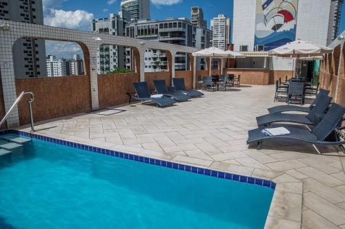 桑托斯大西洋公寓酒店的一座大楼内的游泳池,配有椅子和遮阳伞