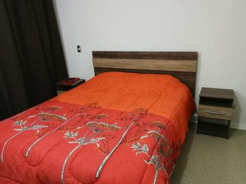 圣地亚哥Departamento santiago的一张带橙色棉被和木制床头板的床