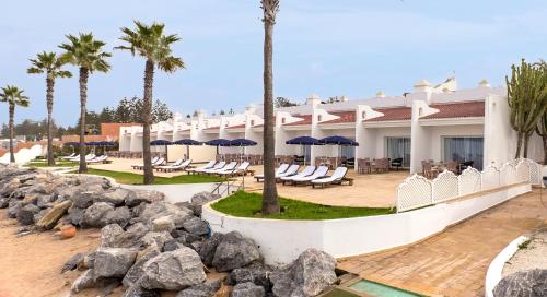 斯希拉特安菲特里特宫度假酒店及Spa的一个带椅子和遮阳伞及棕榈树的度假村