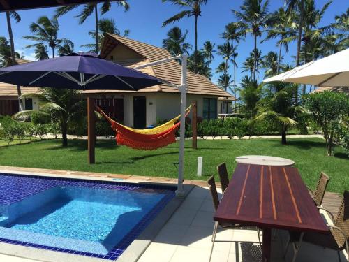 普拉亚多斯卡内罗斯Bangalô luxo Carneiros Beach Resort的游泳池旁的吊床,配有桌子和遮阳伞