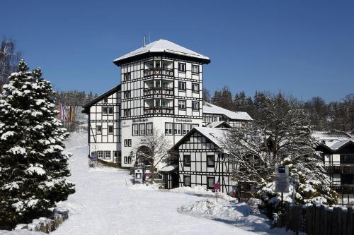 温特贝格Dorint Resort Winterberg的雪中一座大建筑,有圣诞树
