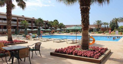 托罗埃利亚-德蒙特格里Hotel Clipper - EL DELFÍN VERDE RESORTS - Platja de Pals的一个带桌椅的度假村游泳池,并种植了棕榈树