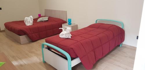阿尔巴Cristallo Camere的宿舍间的两张床,配有红色床单和白色毛巾
