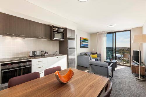 悉尼悉尼奥林匹克公园凯斯特公寓式酒店的厨房以及带桌椅的起居室。