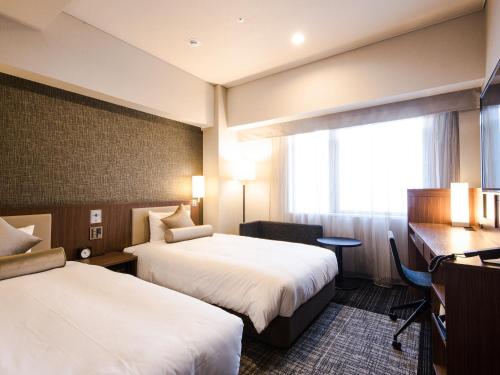 横滨UNIZO酒店 - 横滨站西(HOTEL UNIZO Yokohamaeki-West)的酒店客房设有两张床、一张书桌和一个窗户。