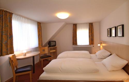 特里尔Hotel Haus am Berg的酒店客房设有两张床、一张桌子和一张书桌。