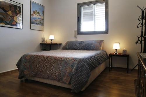 荷兹利亚Herzelia Rooftop Special 2 Room Apartment的一间卧室配有一张床、一个窗口和两盏灯。