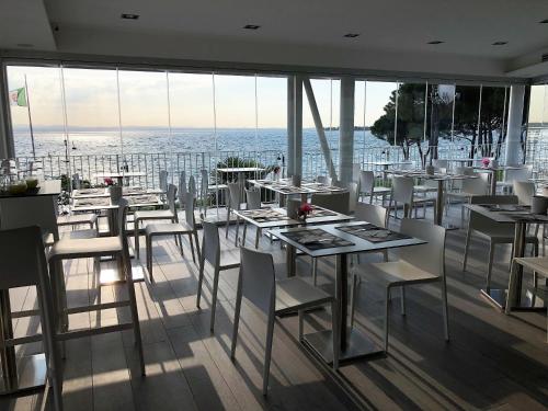 西尔米奥奈卡塞雷娜酒店的餐厅设有白色的桌子和白色的椅子及窗户。